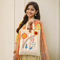 Woman holding a tote bag with colorful designs against a plain background