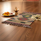 Decorative mat with geometric pattern on a wooden floor, accompanied by a small plate of flowers and a lit candle.