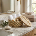 Woven basket with lid on a marble countertop with towels and soap.