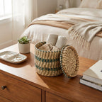 Woven basket with folded clothes on a wooden dresser next to a bed with beige bedding.