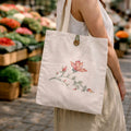 Person holding a tote bag with floral design at an outdoor market.