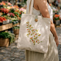 Person holding a tote bag with leaf design in an outdoor market setting