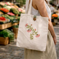Person holding a tote bag with floral design at an outdoor market.