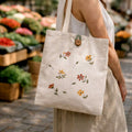 Person holding a tote bag with floral designs in an outdoor market setting