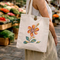 Person holding a tote bag with a floral design at an outdoor market.