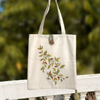 Tote bag with leaf design hanging on a wooden railing with a blurred green background
