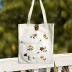 White tote bag with floral designs on a wooden railing with a blurred green background
