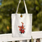 White tote bag with floral design hanging on a wooden railing with a blurred green background