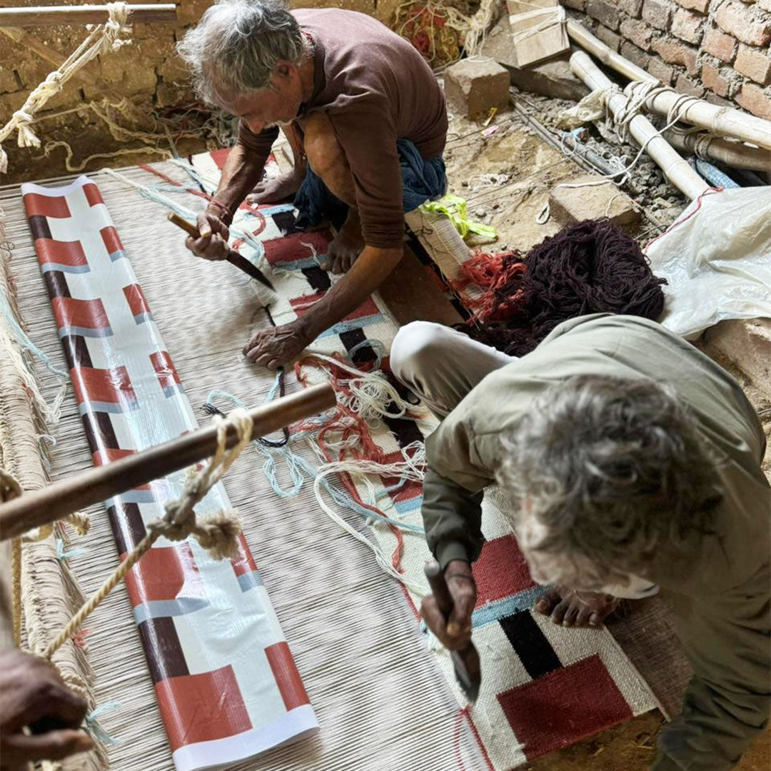 Artisans working on a traditional loom with a patterned fabric.