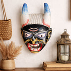 Decorative mask with horns on a wall next to a lantern and books