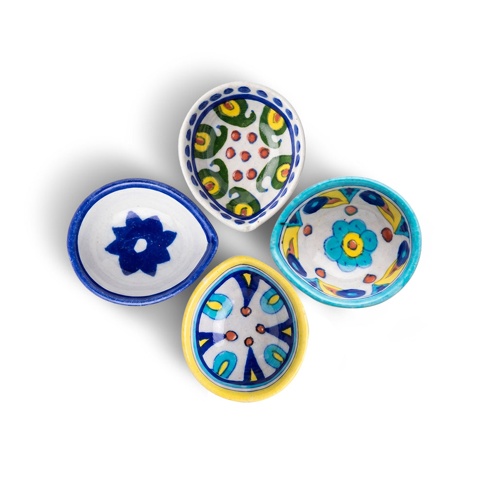 Set of 4 assorted handcrafted blue pottery diyas arranged in a circular flower layout on a white background