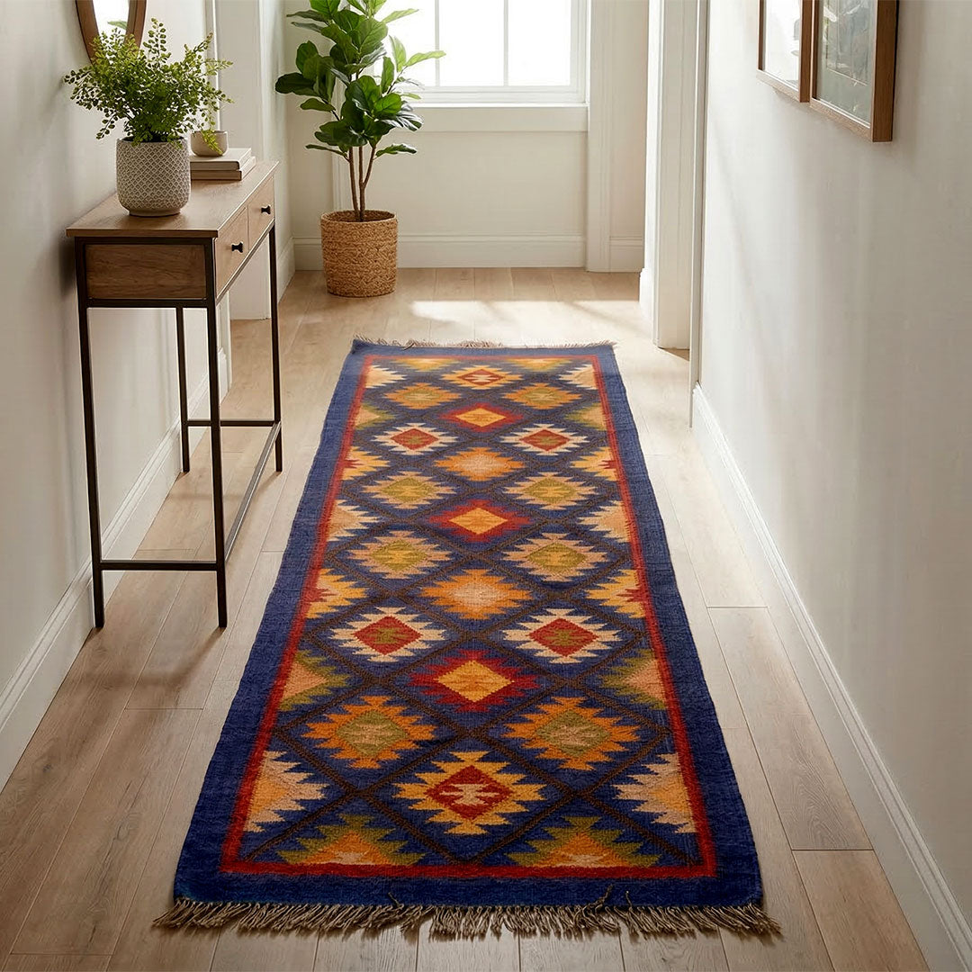 Colorful patterned rug on a wooden floor in a room with plants and a desk.