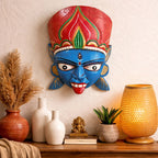Decorative mask with red and blue colors on a wall above a wooden shelf with decorative items.