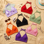 Collection of vibrant hand-crocheted halter bikini tops in various colors displayed on sand.