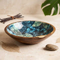 Botanical enamel printed mango wood serving bowl with gold leaf accent resting on a neutral stone table next to dried botanicals