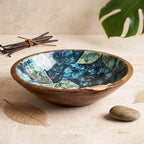 Botanical enamel printed mango wood serving bowl with gold leaf accent resting on a neutral stone table next to dried botanicals