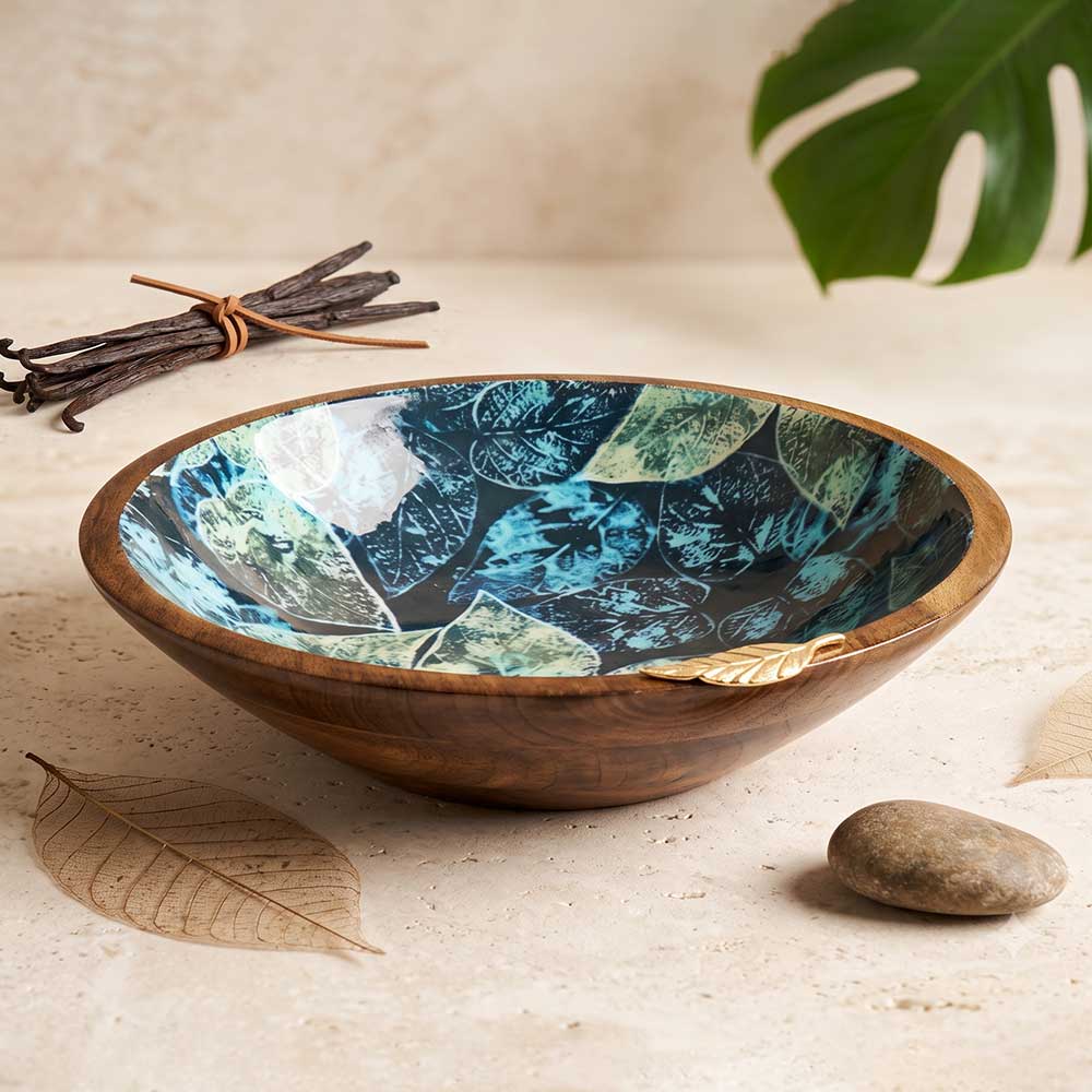 Botanical enamel printed mango wood serving bowl with gold leaf accent resting on a neutral stone table next to dried botanicals