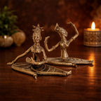 Bronze statues of two figures on a wooden surface with a candle in the background