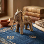 Bronze elephant figurine on a blue embroidered fabric with books and a candle in the background.