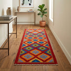 Colorful geometric-patterned rug on a wooden floor with a plant and tables in the background.