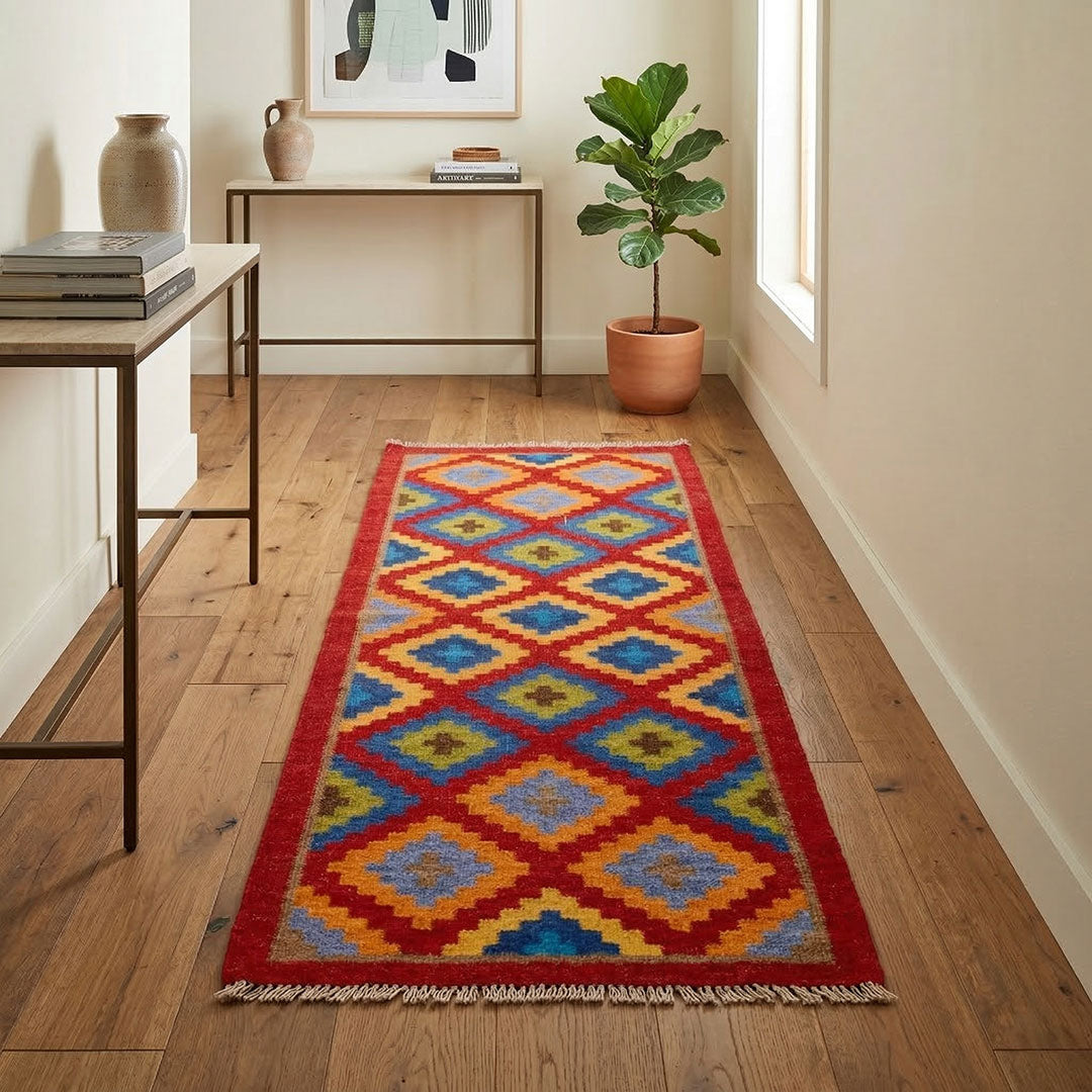 Colorful geometric-patterned rug on a wooden floor with a plant and tables in the background.