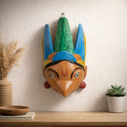  mask with blue and green feathers on a wall above a wooden shelf.