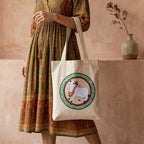 Person wearing a patterned dress holding a tote bag with a decorative design.