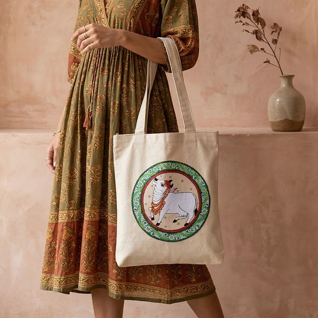 Person wearing a patterned dress holding a tote bag with a decorative design.