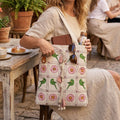 Person holding a patterned bag with a wooden table and plants in the background
