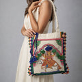 Woman holding a decorative handbag with intricate designs and tassels against a gray background