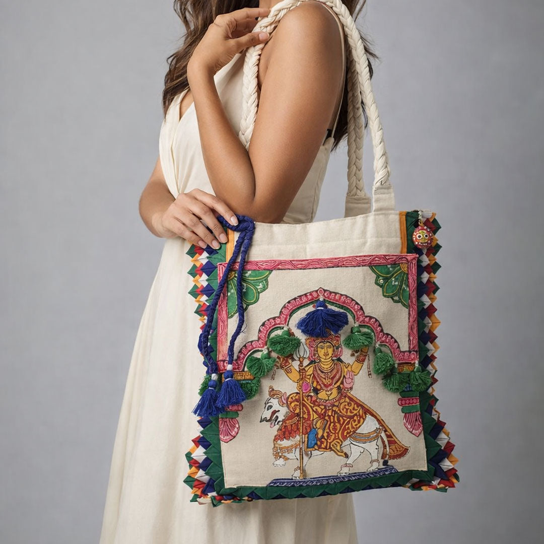 Woman holding a decorative handbag with intricate designs and tassels against a gray background