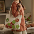Person holding a tote bag with decorative designs in a home setting
