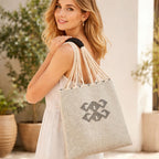 Woman holding a gray tote bag with a decorative black design in an indoor setting with plants.