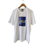 Front view of a white pure cotton hand-painted t-shirt with a moon over the ocean graphic design hanging on a wooden hanger.