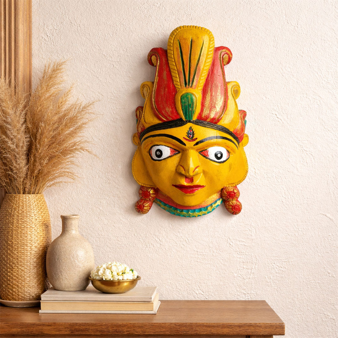 Decorative mask on a wall above a wooden shelf with decorative items.