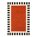 A luxurious hand-tufted New Zealand wool rug featuring a deep burnt-orange center and a black-and-cream striped border, viewed from a top-down flat perspective.