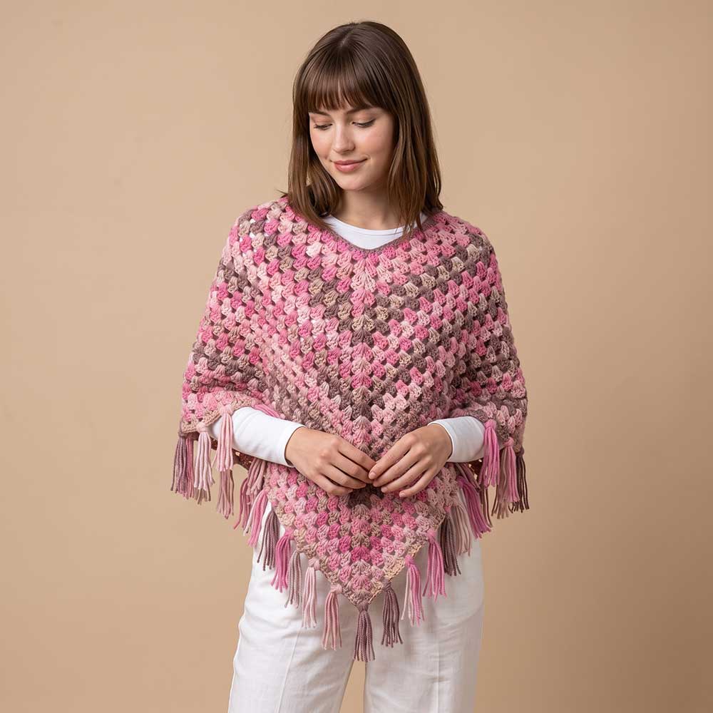 Model in studio wearing handmade pink and taupe crochet poncho over a white long-sleeve shirt