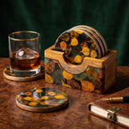 A set of artisan mango wood coasters with autumn leaf enamel print inside a wooden holder on a wooden desk.