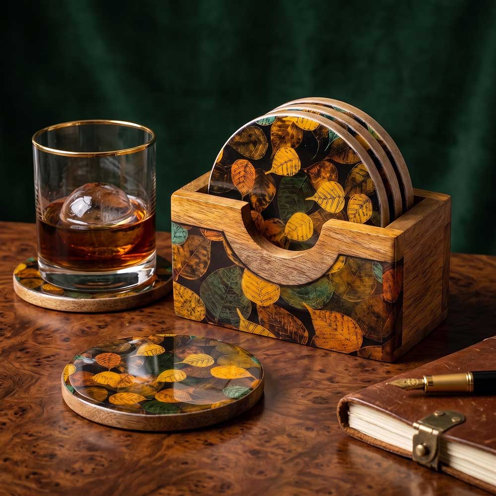 A set of artisan mango wood coasters with autumn leaf enamel print inside a wooden holder on a wooden desk.