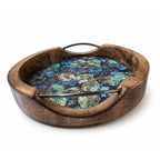 Overhead view of a round mango wood serving tray showing intricate botanical leaf enamel print and metal handles.