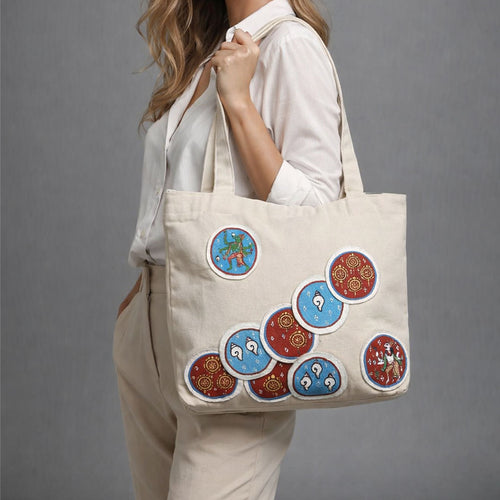 Person holding a beige tote bag with colorful circular designs on a gray background