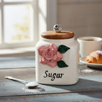 Decorative sugar jar with floral design and wooden lid on a table with coffee and pastries.
