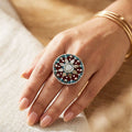 Close-up of a hand wearing a decorative ring with a floral design on a neutral background
